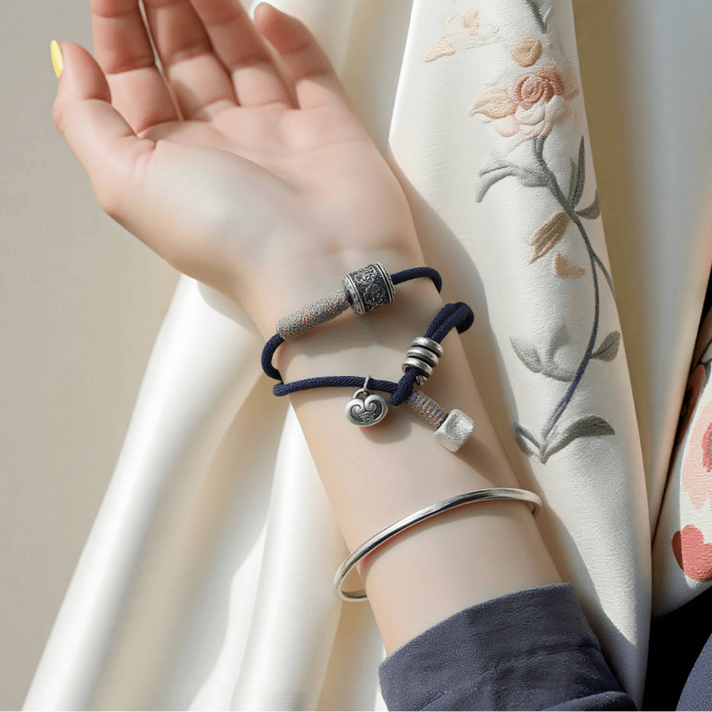 Six-Word Mantra Blue Thread Bracelet worn on wrist with silver charm details, resting against embroidered fabric, symbolizing protection and mindful focus in work mode.