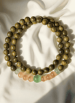 Green Sandalwood & Cat’s Eye Buddha Bracelet laid on soft ivory fabric, featuring warm wood tones and calming gemstone accents, ideal for emotional reset in off-mode evening rituals.