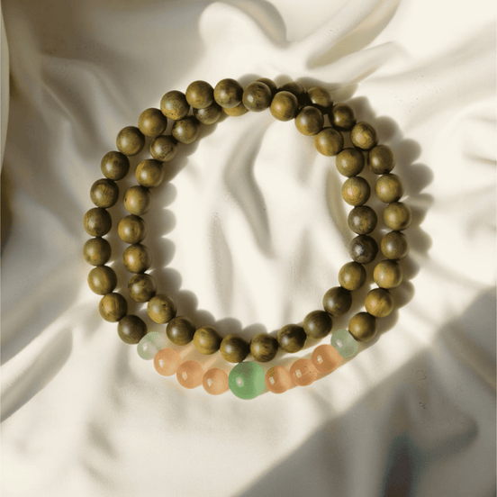 Green Sandalwood & Cat’s Eye Buddha Bracelet laid on soft ivory fabric, featuring warm wood tones and calming gemstone accents, ideal for emotional reset in off-mode evening rituals.